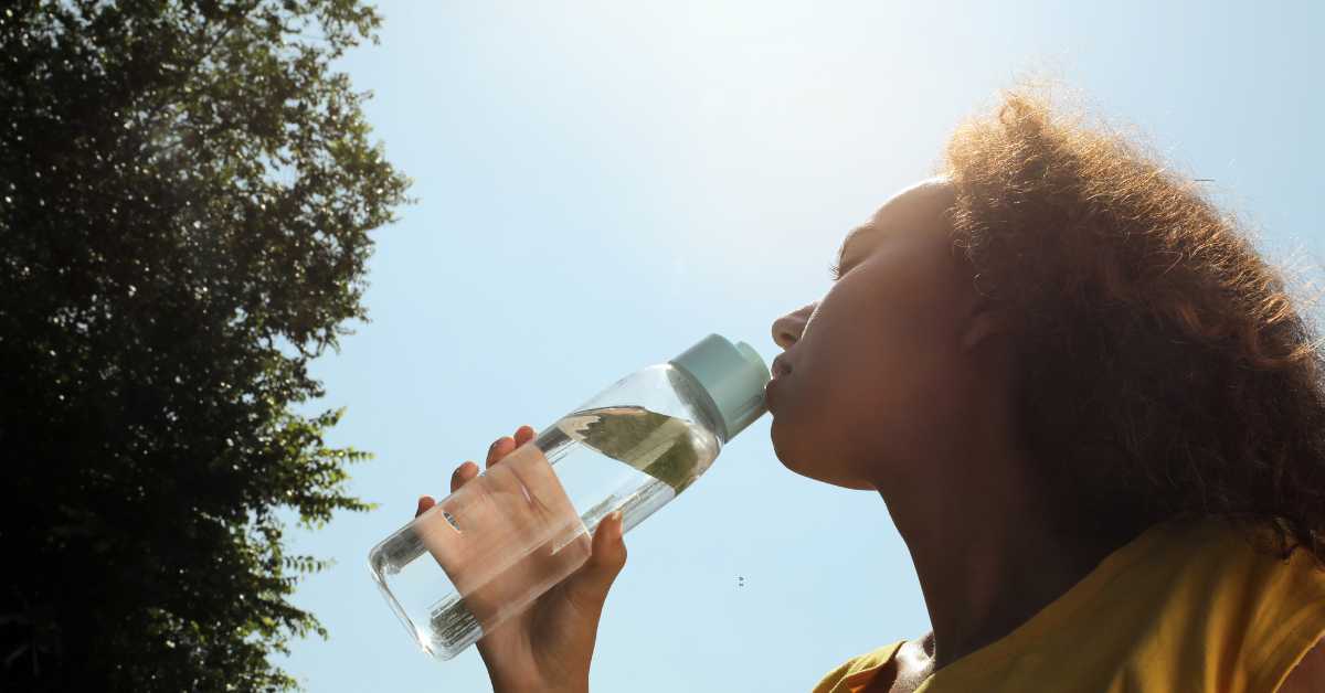 Erschöpfte Person trinkt Wasser an einem heißen Tag