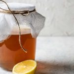 Glas Kombucha mit sichtbarem SCOBY im Hintergrund