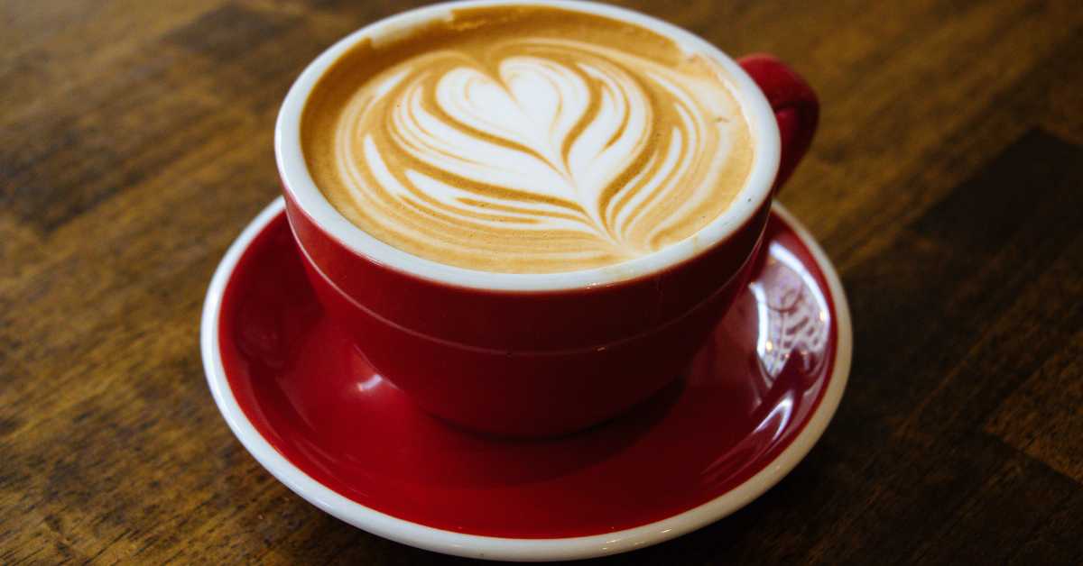 Tasse Kaffee mit Uhr im Hintergrund als Symbol für Koffeinwirkung und Timing